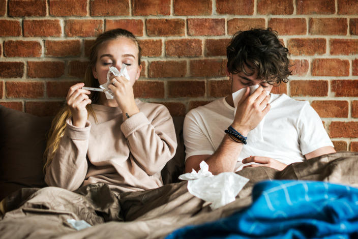 Paar sitzt erkältet im Bett und benutzt Taschentücher