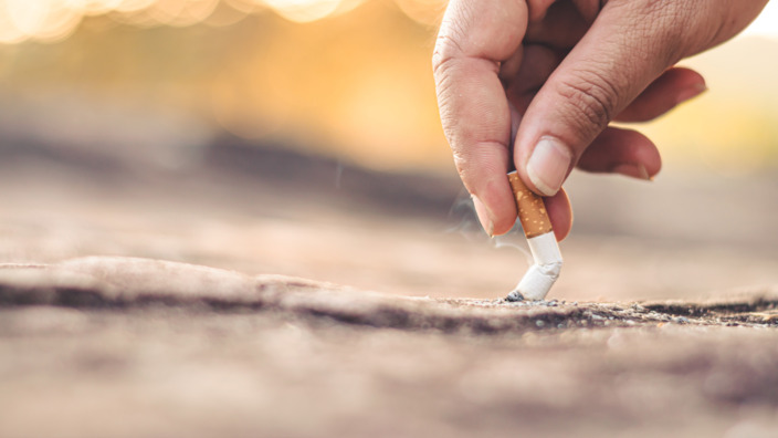 Mann drückt einen Zigarettenstümmel am Boden aus