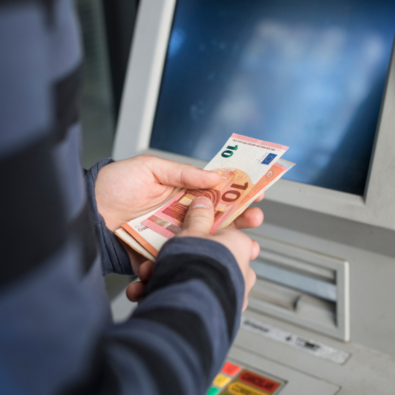 Person mit Geldscheinen in der Hand steht vor einem Geldautomat