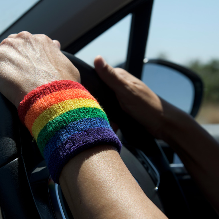 Person mit regenbogenfarbenen Armband sitzt am Lenkrad.