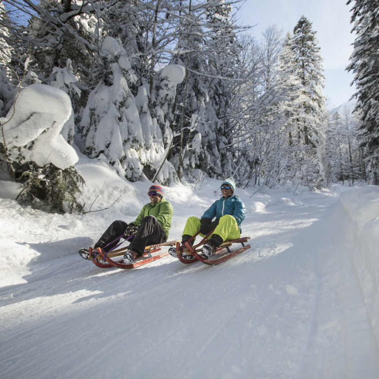 Zwei Personen auf Rodeln in verschneiter Winterlandschaft