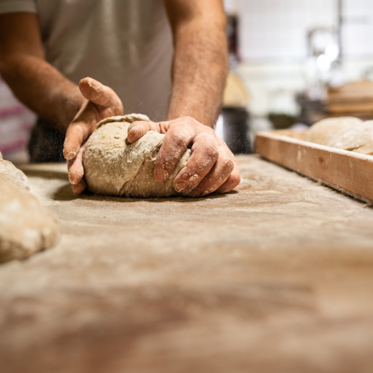 Bäcker verarbeitet einen Vollkornteig zu Brotlaiben