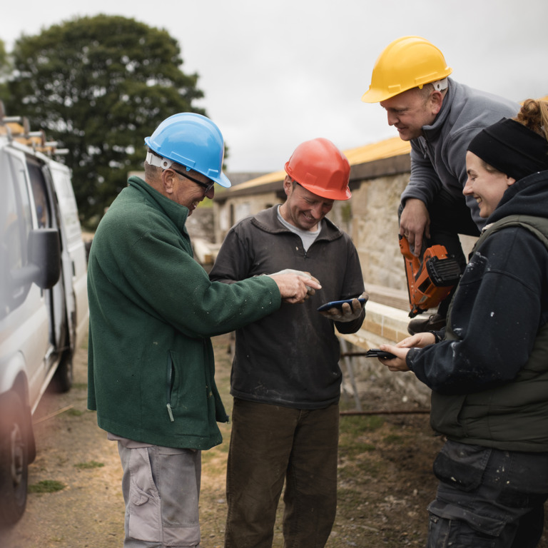 Gruppe Handwerker mit Helmen auf Baustelle schauen auf ein Smartphone