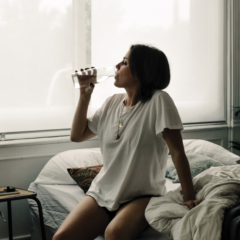 Frau sitzt auf dem Bett und trinkt Wasser