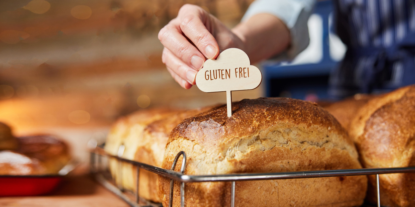 Jemand steckt ein Schild mit "Gluten frei" in ein Brot