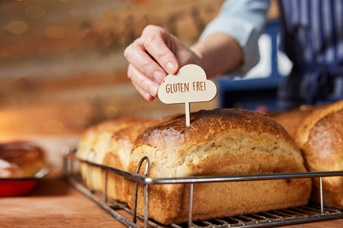 Jemand steckt ein mit glutenfrei beschriftetes Schild in ein Brot