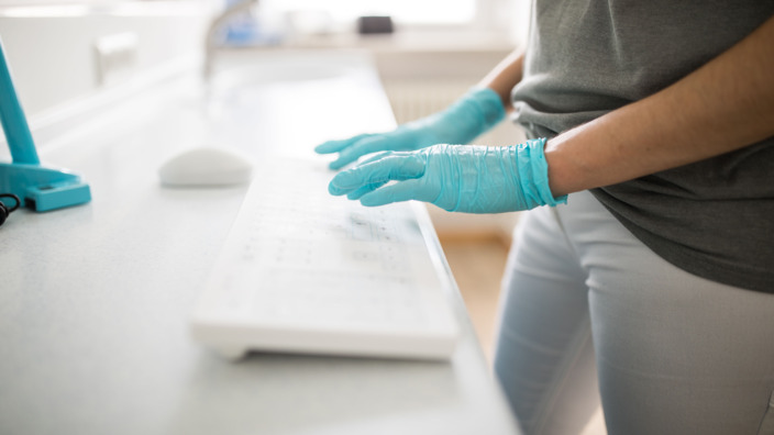 Eine Ärztin trägt Handschuhe und tippt etwas über die Computertastatur ein.