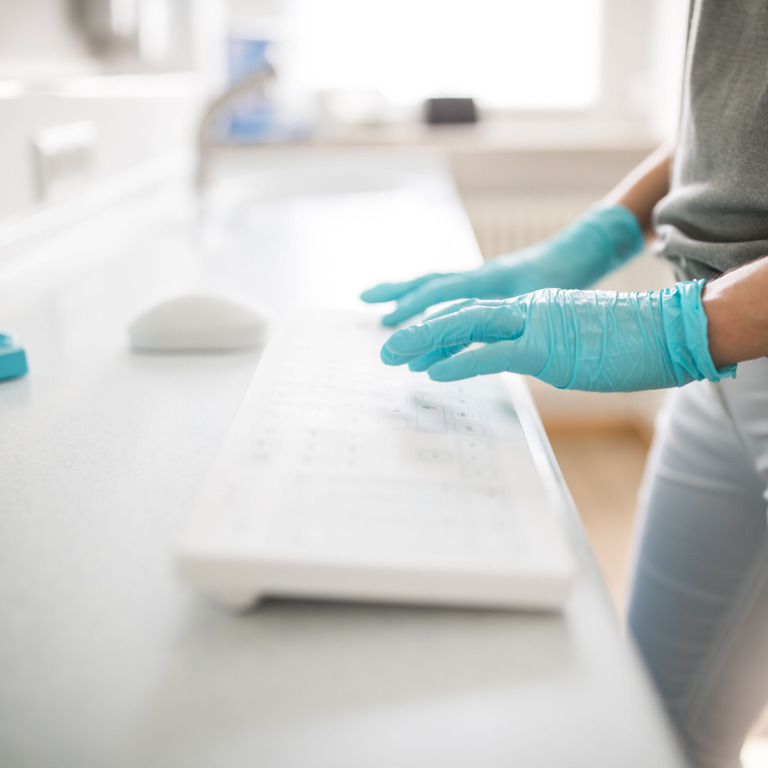 Person mit medizinischen Handschuhen gibt etwas auf Tastatur ein.