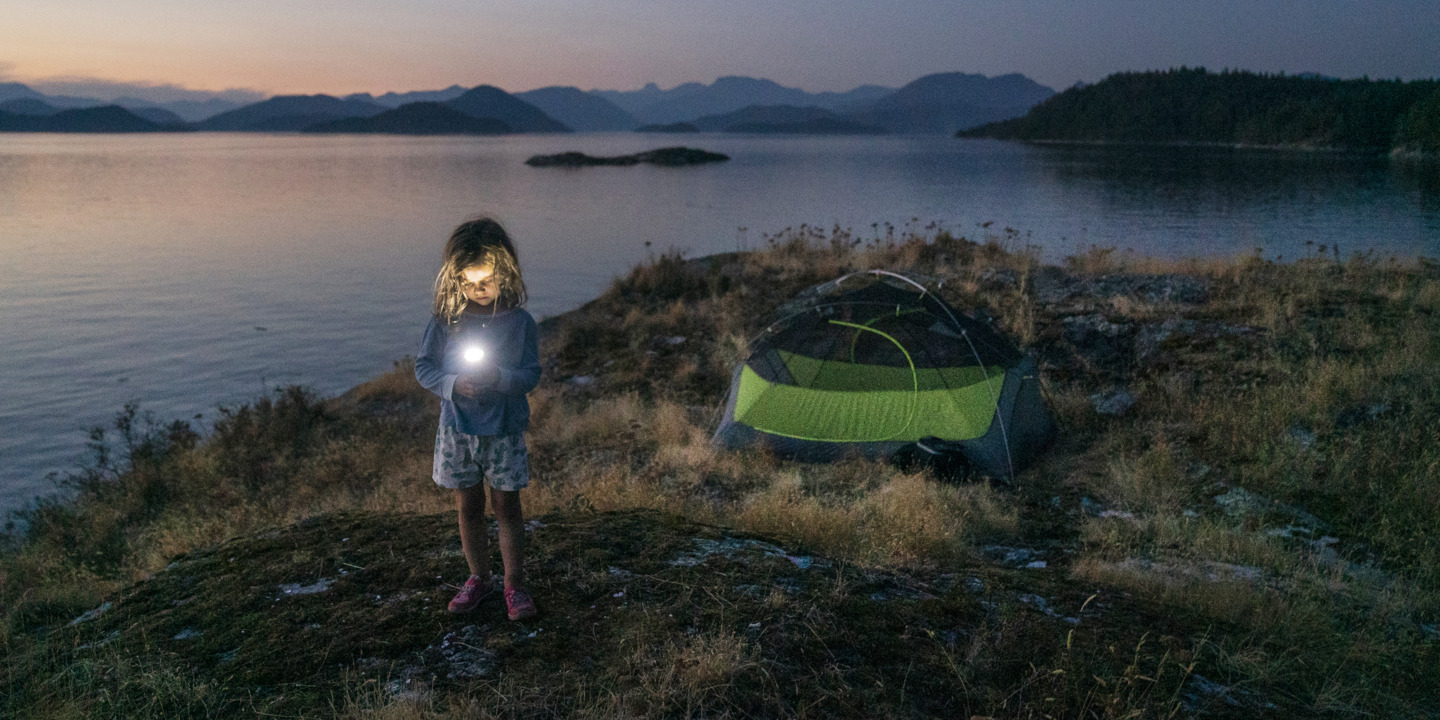 Kind steht mit Taschenlampe am nächtlichen See