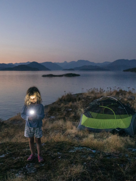 Kind steht mit Taschenlampe am nächtlichen See