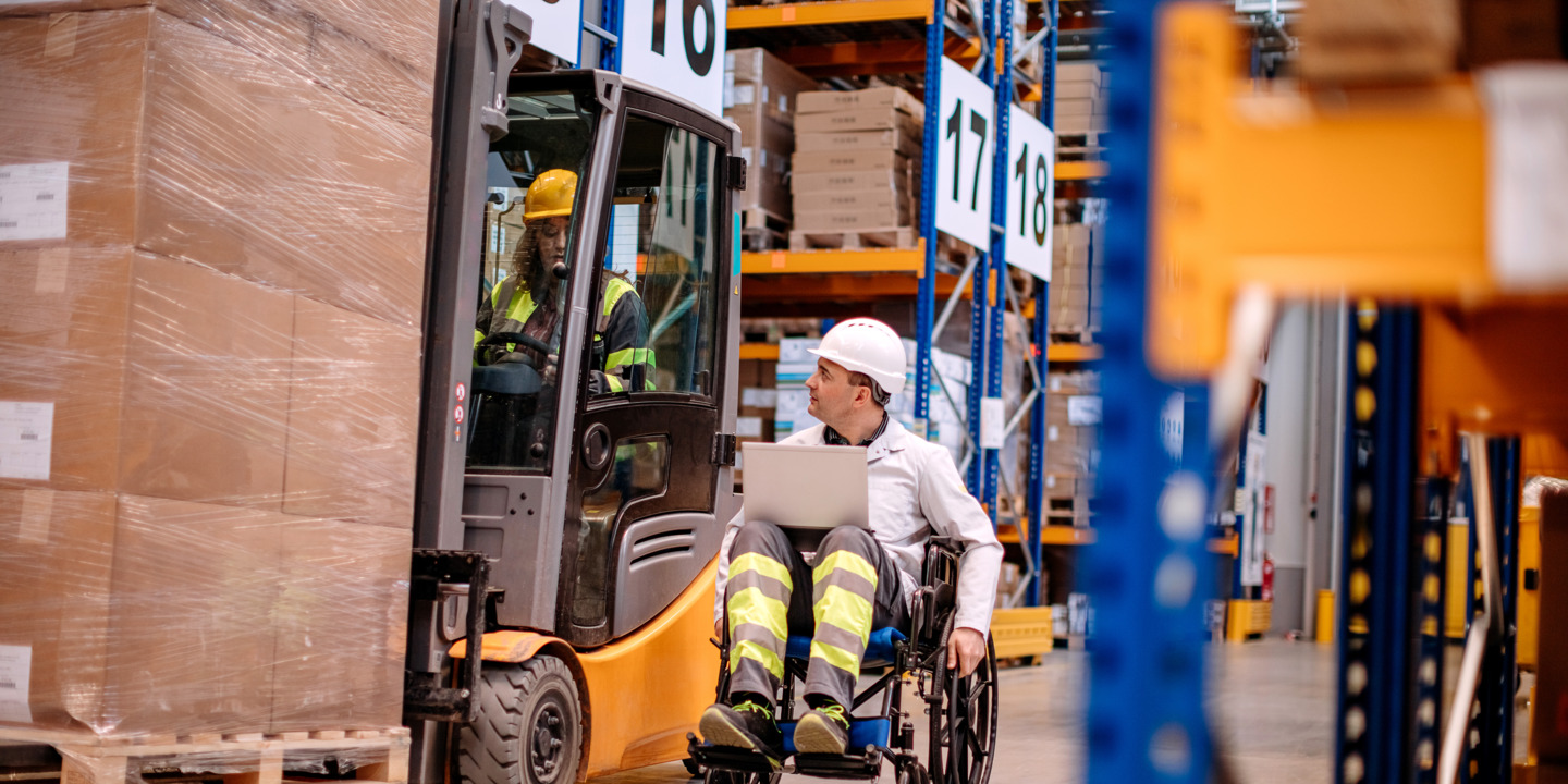Ein Mann sitzt im Rollstuhl und fährt durch eine Fabrikhalle. 