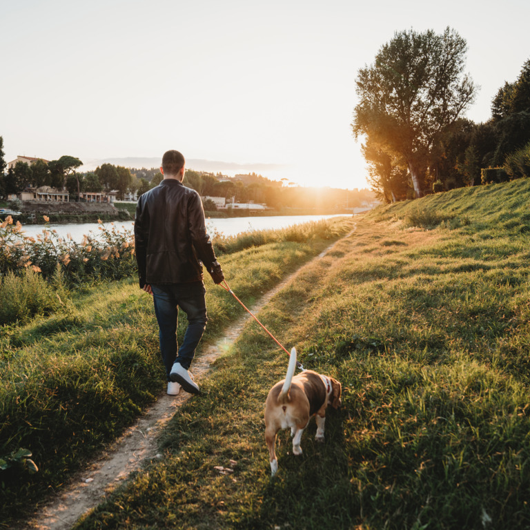 Mann geht an einem Fluss mit Hund spazieren.