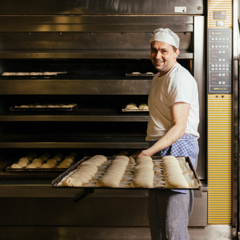 Bäcker holt Brötchen aus dem Ofen