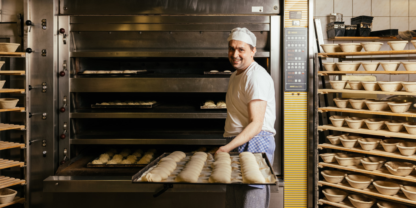 Bäcker in Goldbrötchen Bäckerei holt Brötchen aus dem Ofen