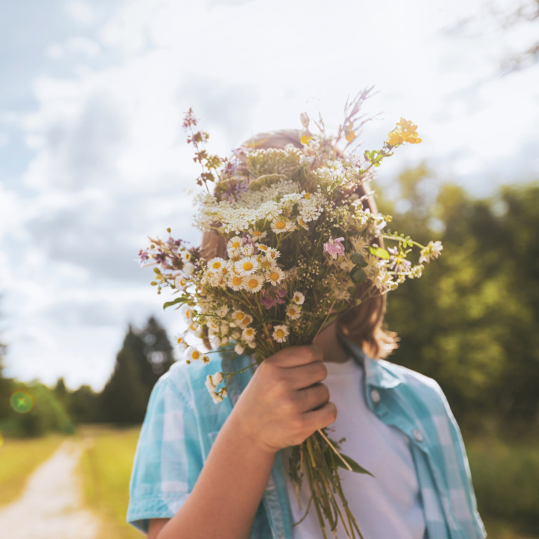 Kind hält einen Blumenstrauss vor sein Gesicht