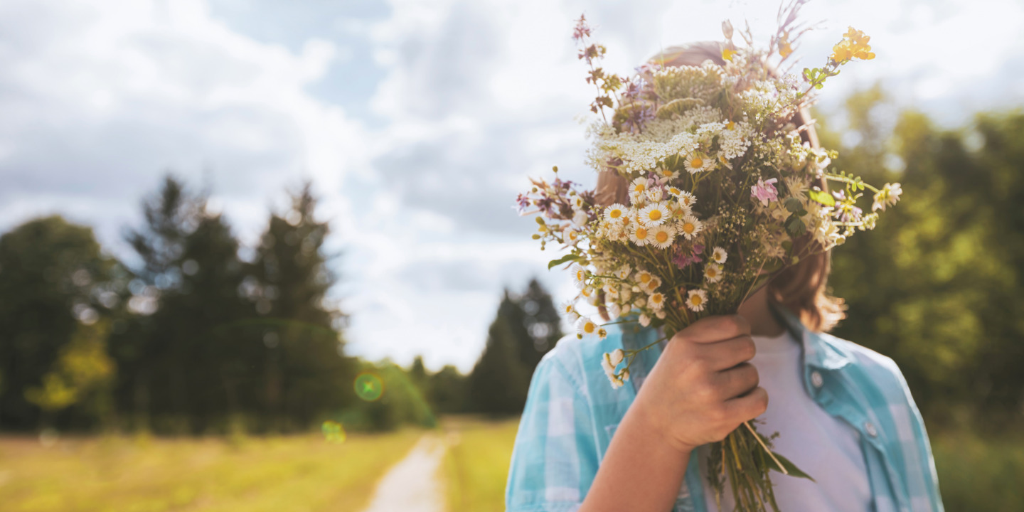 Kind hält einen Blumenstrauss vor seinem Gesicht