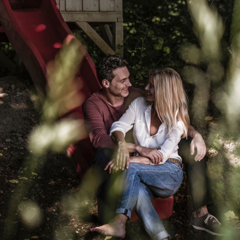 Frau und Mann sitzen innig auf einer Rutsche auf einem Spielplatz.