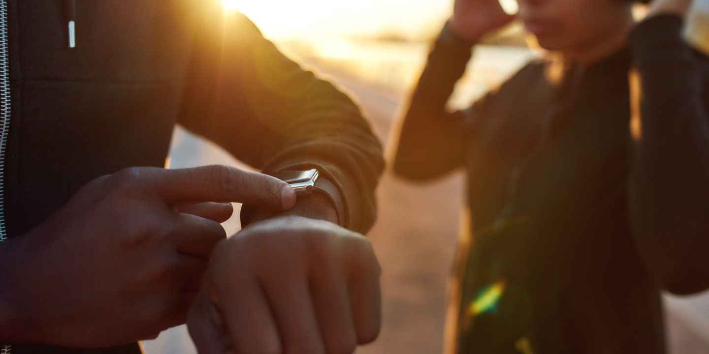 Junge Menschen im Sonnenuntergang schauen auf Fitnesstracker und nutzen Fitness-Apps