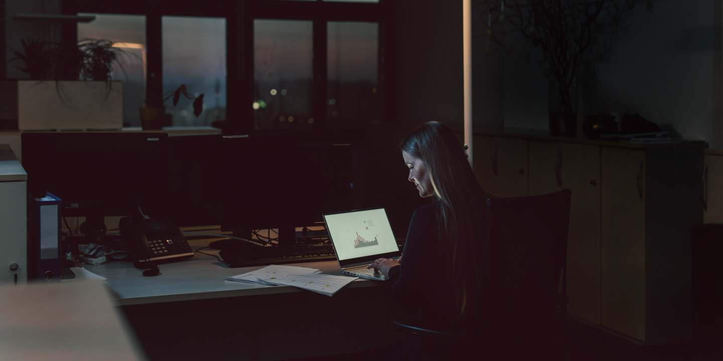 Frau, die abends im Büro vor dem Laptop sitzt.