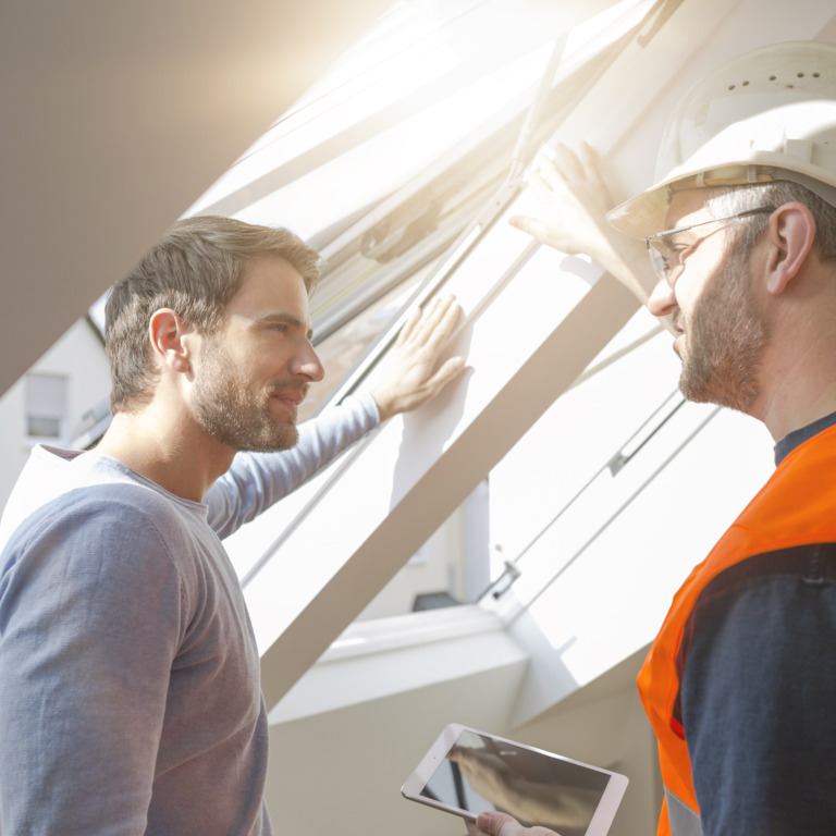 Handwerker und Kunde stehen gemeinsam an einem offenen Fenster