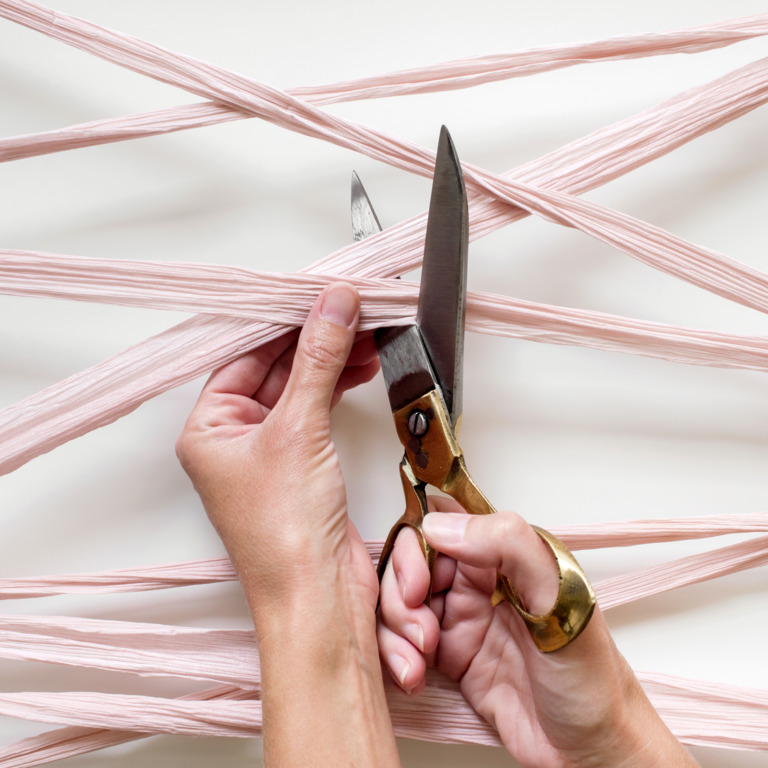 Schere in der Hand durchschneidet rosa Bänder