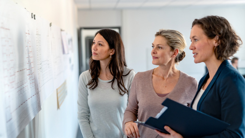 Drei Frauen, die auf einen Plan an der Wand schauen.