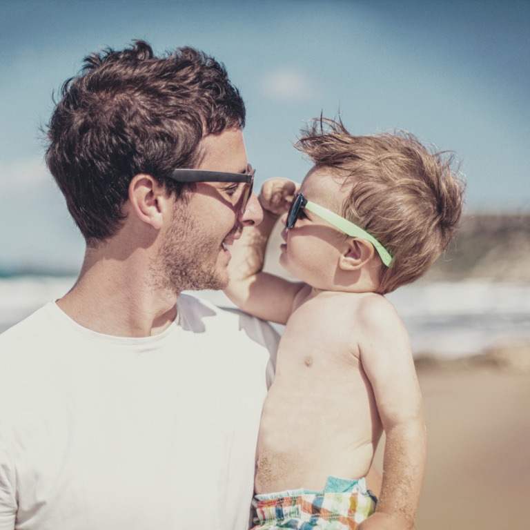 Vater und Sohn schauen sich durch die Sonnenbrillen am Strand an
