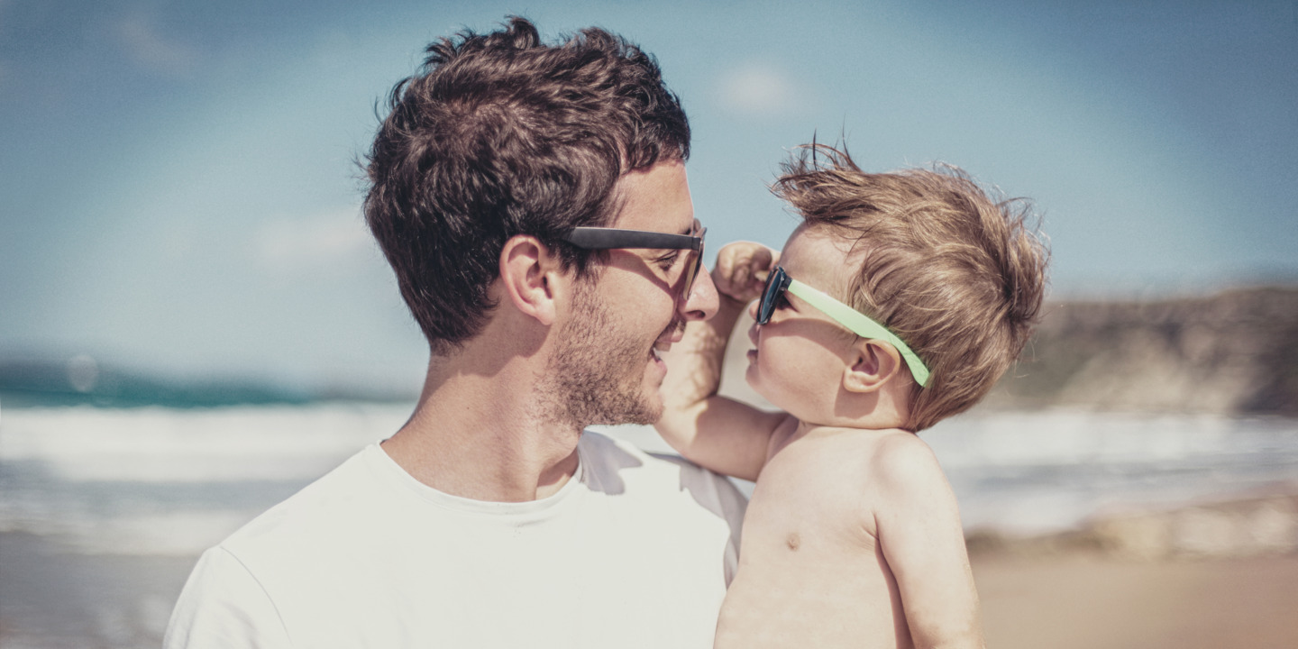 Vater und Sohn schauen sich durch die Sonnenbrillen am Strand an