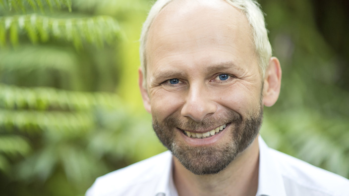 Dr. Jens Förster lächelt vor einem grünen Hintergrund in die Kamera