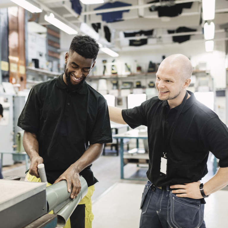 Arbeiter mit Migrationshintergrund unterhält sich mit einem Kollegen in der Produktionshalle