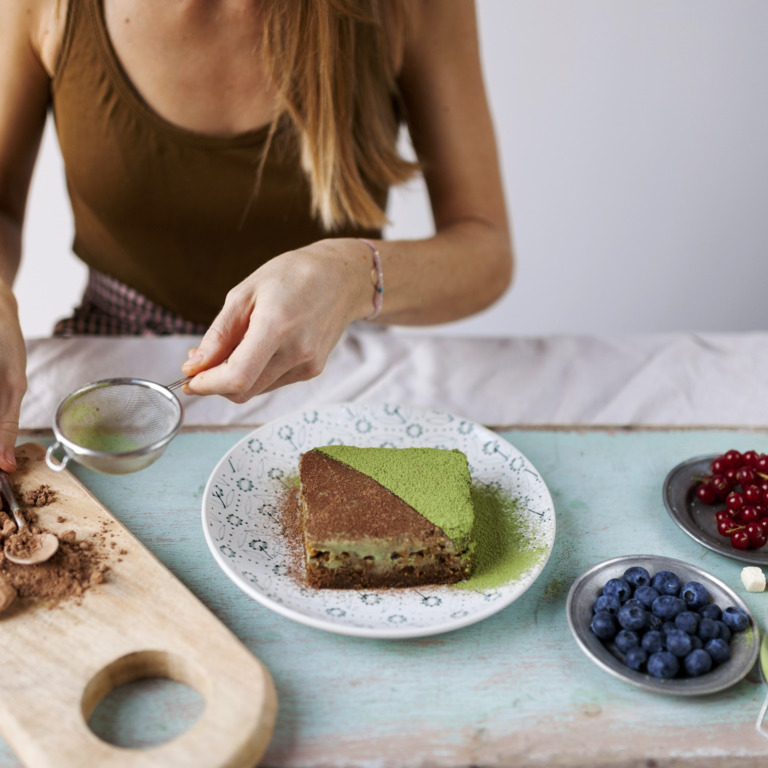 Frau dekoriert veganen Kuchen mit Matcha und Kakaopulver