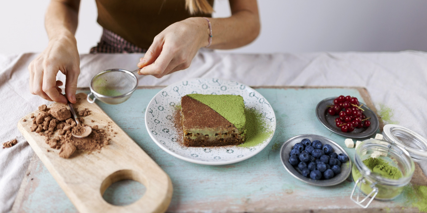 Frau dekoriert veganen Kuchen mit Matcha und Kakaopulver