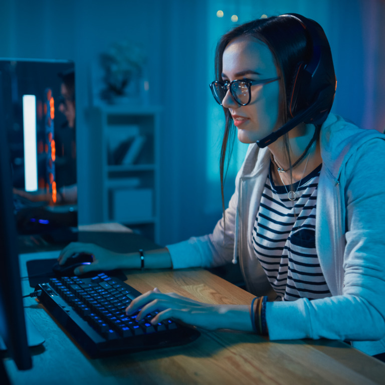 Junge Frau sitzt am Schreibtisch und spielt Computerspiele.