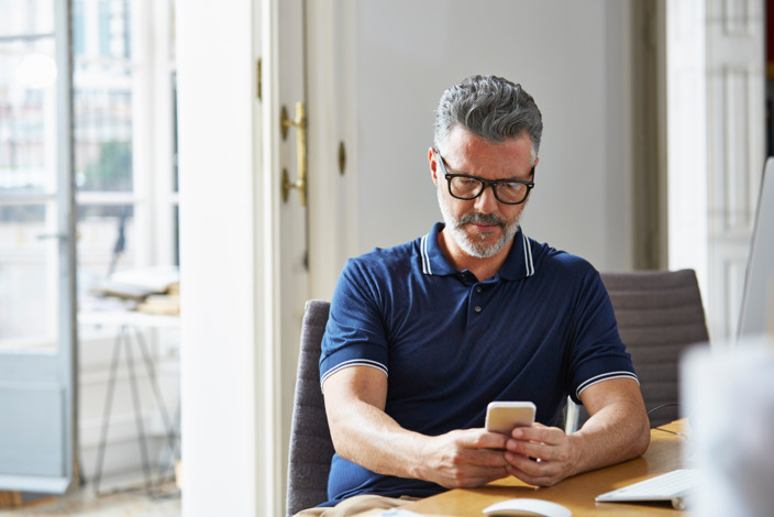 Mann sitzt mit Handy am Tisch