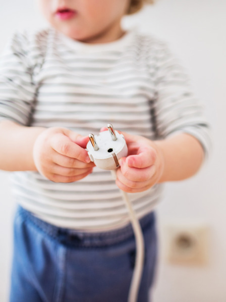 Kleinkind hält den Stecker eines Elektrogerätes in der Hand