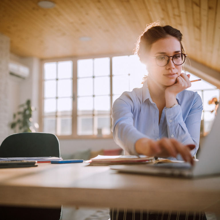 Dunkelhaarige Frau mit Brille sitzt an Laptop im Homeoffice