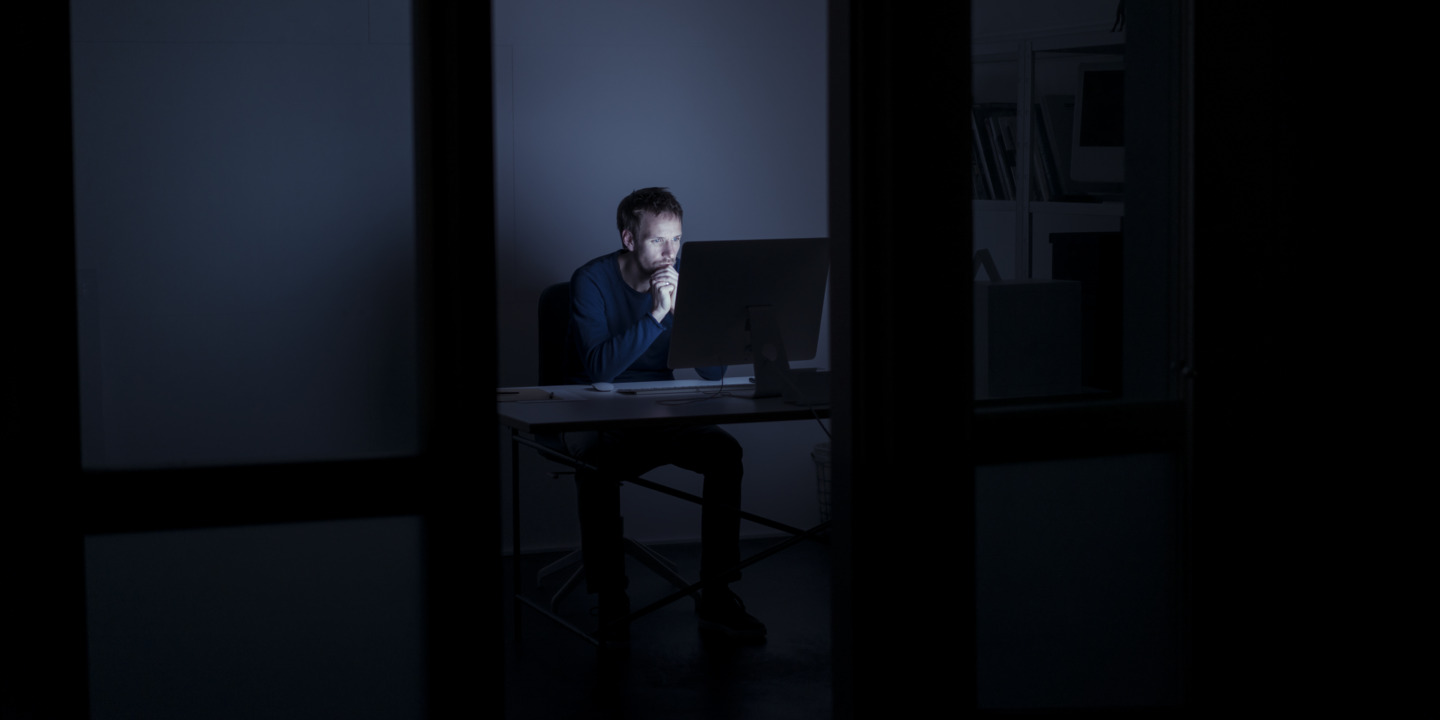 Mann sitzt im dunklen Büro vor dem PC