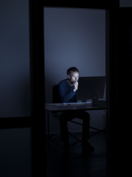 Mann sitzt im dunklen Büro vor dem PC
