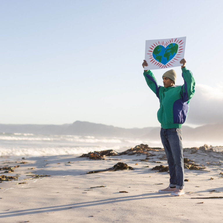 Junger Mann steht am Strand und hält Schild mit Herz hoch