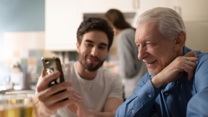 Junger Mann zeigt älteren Herren etwas auf seinem Smartphone.