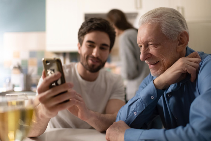 Junger Mann zeigt älteren Herren etwas auf seinem Smartphone.