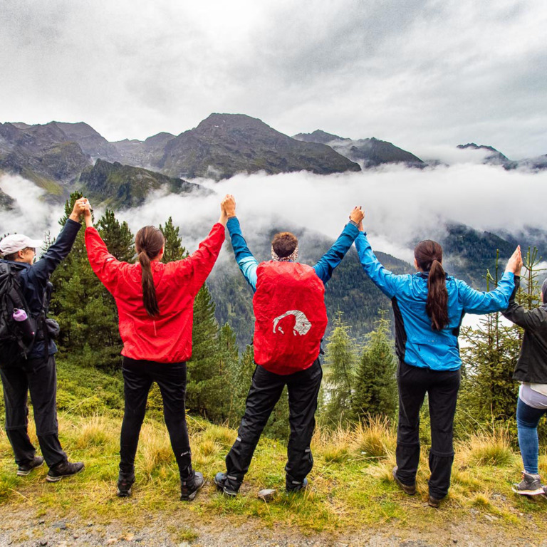 Gruppe aus fünf Leuten steht am Gipfel des Berges und jubelt