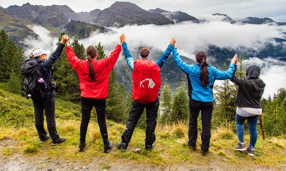 Wandergruppe aus fünf Einheimischen und Geflüchteten steht am Gipfel eines Berges und jubelt