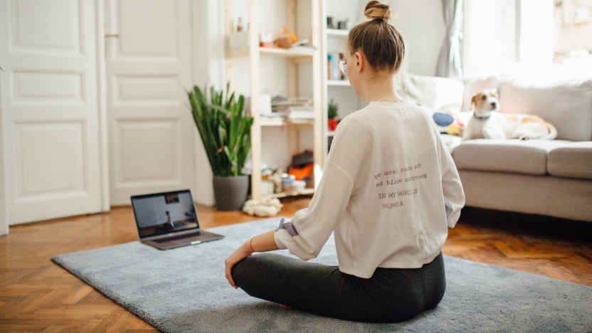 Frau sitzt auf dem Wohnzimmerboden und nimmt an einem Online-Kurs zur Entspannung teil