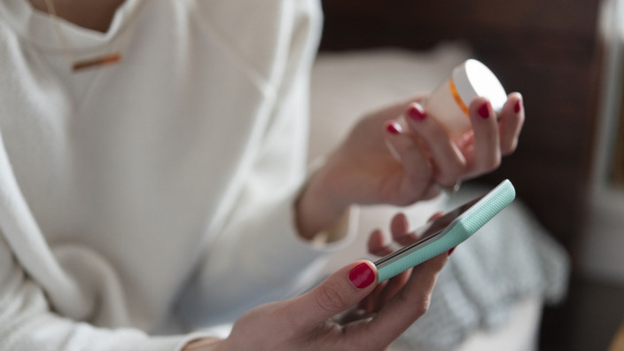 Frau hält Handy und Tablettendose in Händen