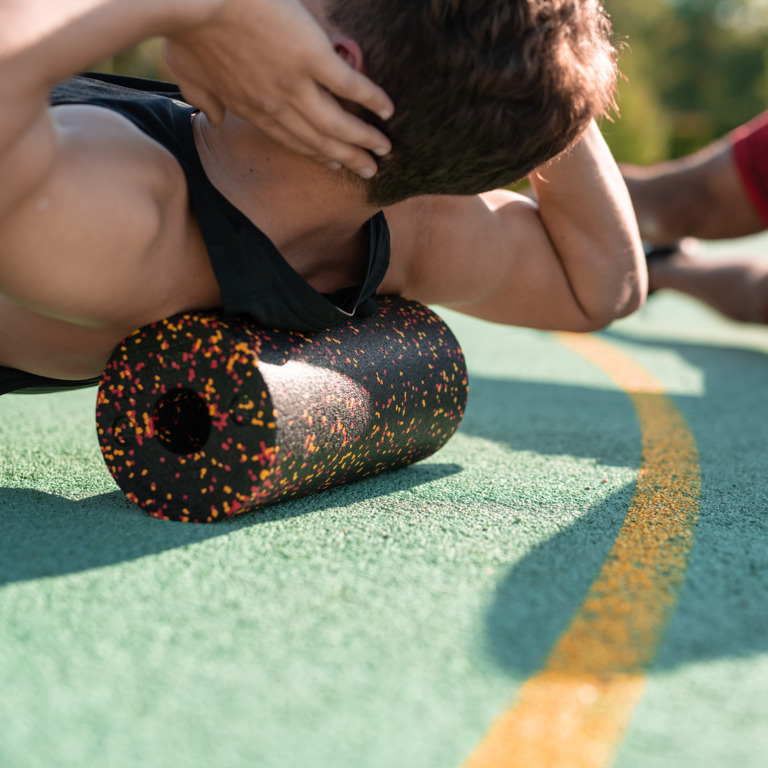 Sportler liegt mit dem oberen Rücken auf einer Faszienrolle