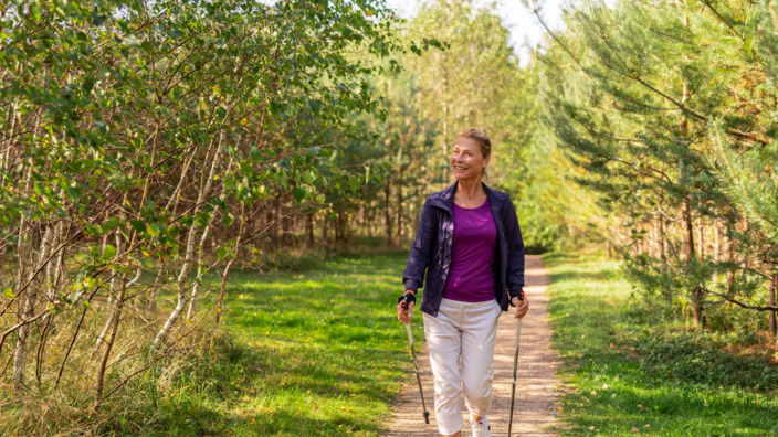 Frau im Sport-Outfit läuft mit Nordic Walking-Stöcken durch den Wald