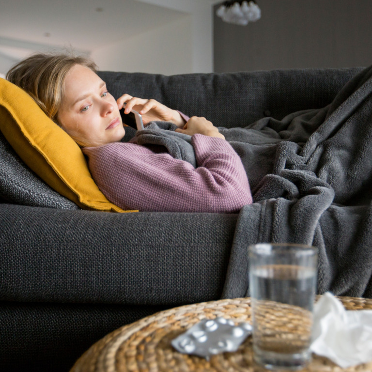 Frau liegt krank auf dem Sofa und telefoniert