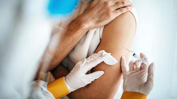 Mann bekommt durch einen Arzt eine Corona-Impfung in den Arm