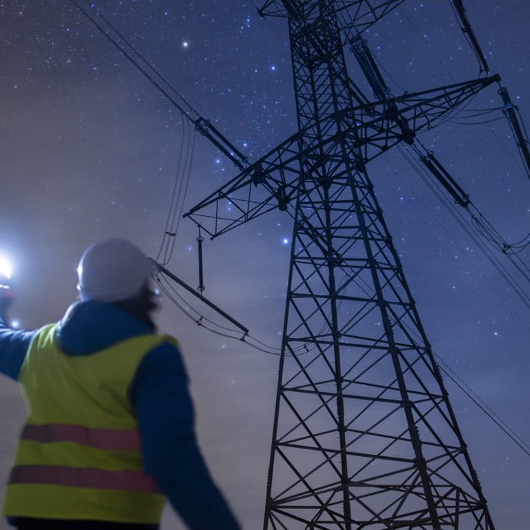 Arbeiter steht in der Nacht mit einer Leuchte vor Strommast.